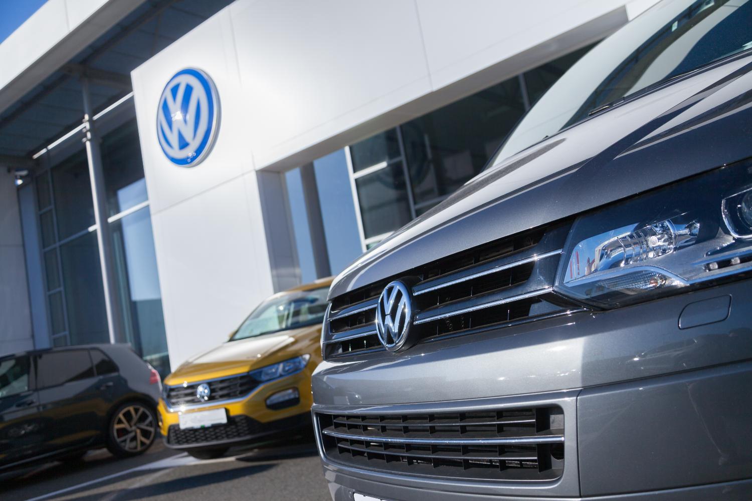 New Volkswagen vehicles parked outside a dealership beneath the Volkswagen emblem.