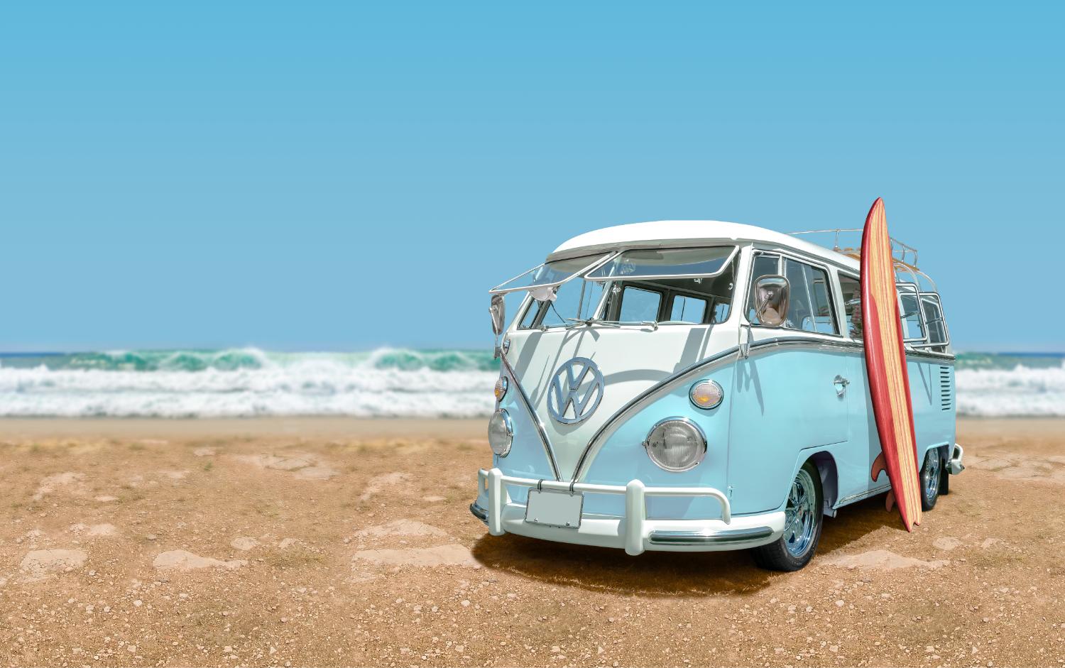 A vintage Volkswagen camper van parked on a beach with a surfboard against its side.