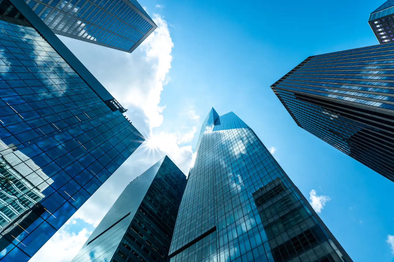 Glass-and-steel office towers photographed from street level, converging upward against a bright blue sky.